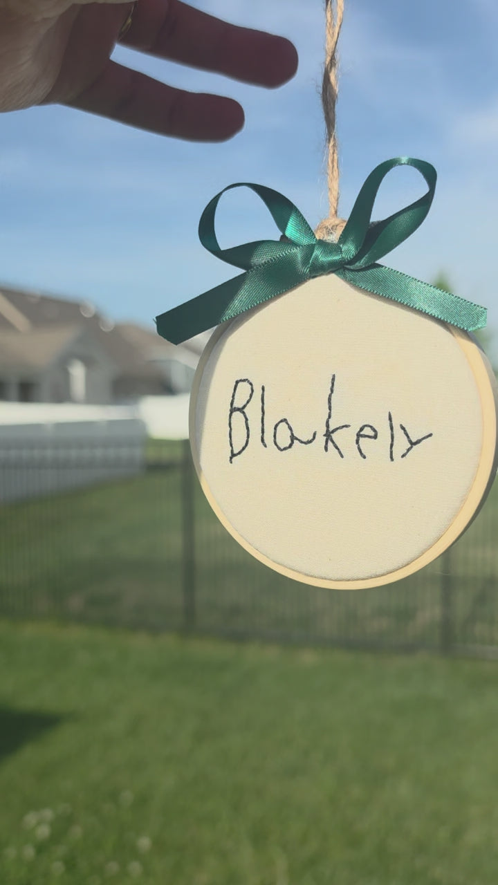 hand embroidered child's signature on a linen hoop ornament with a green bow