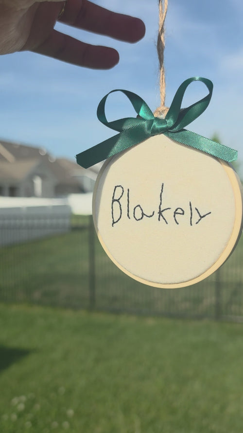 hand embroidered child's signature on a linen hoop ornament with a green bow